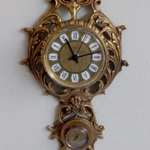 Λεπτομέρεια Αντίκα Μπρούτζινου Ρολογιού Τοίχου Υγρασιόμετρο Αντίκα μπρούτζινο ρολόι τοίχου σε λευκό τοίχο, με ενσωματωμένο θερμόμετρο και υγρασιόμετρο, ύψους 58 εκατοστών.